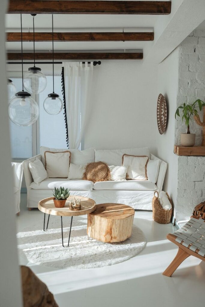  Bright living room with white sofas, wooden tables, and wicker accents under exposed wooden beams.