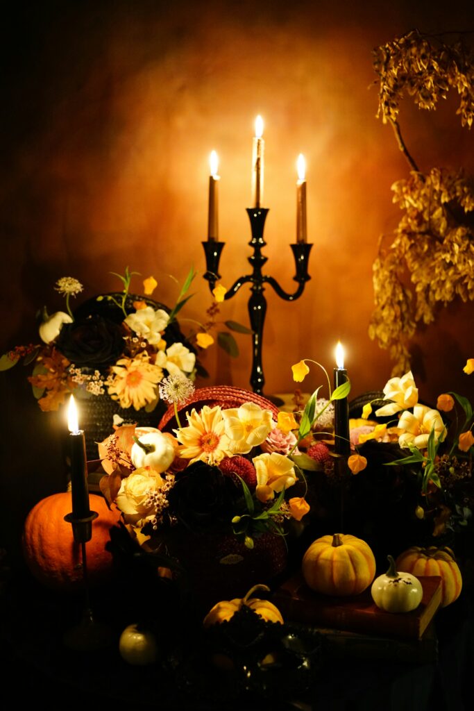 A black candelabra with lit candles surrounded by colorful autumn flowers and decorative pumpkins